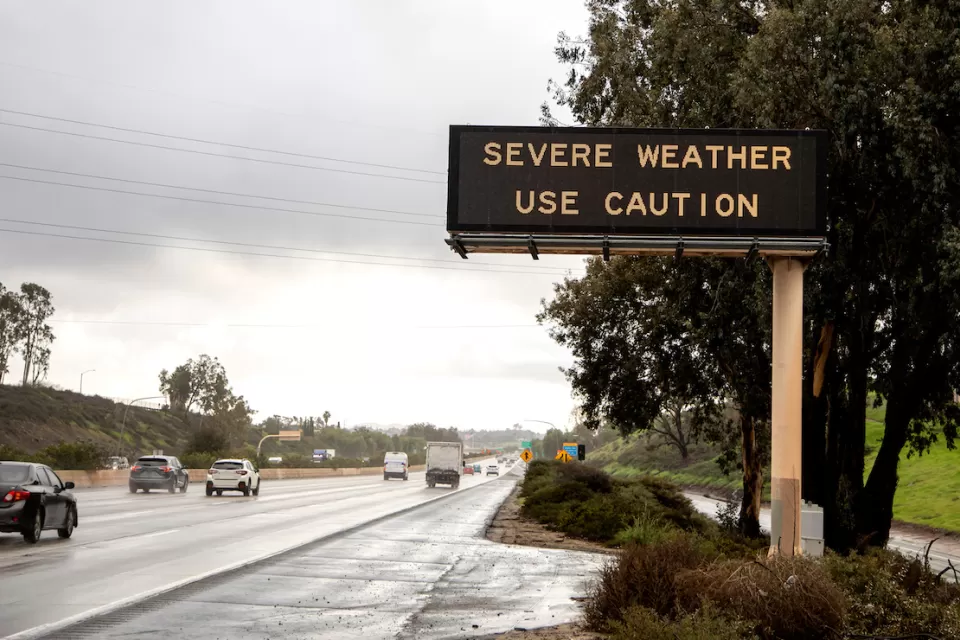 Freeway sign with "severe weather - use caution" over multilane freeway in rainy weather.